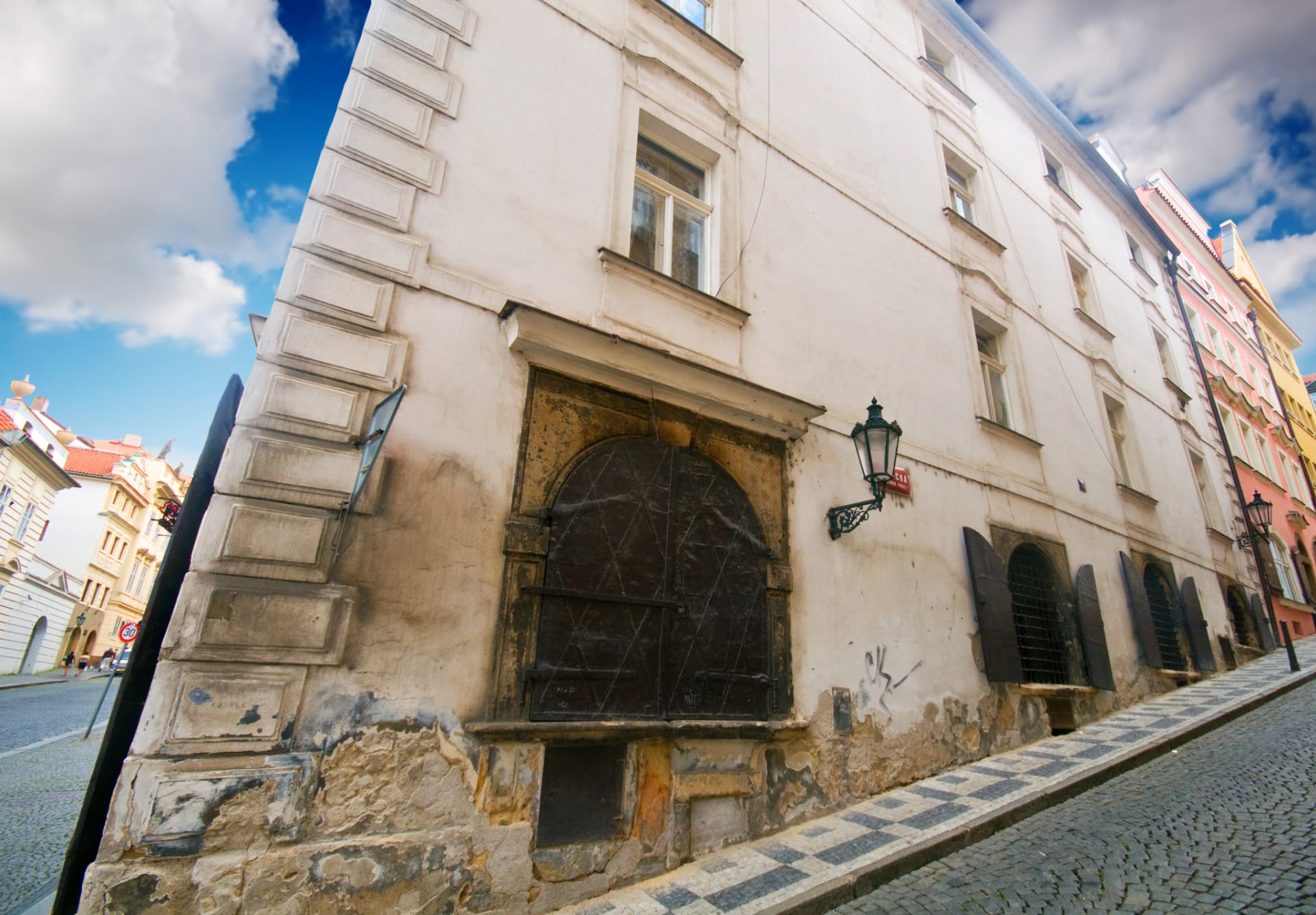 Cobbled Prague street with an old iron-shuttered arched doorway and a wrought-iron lantern